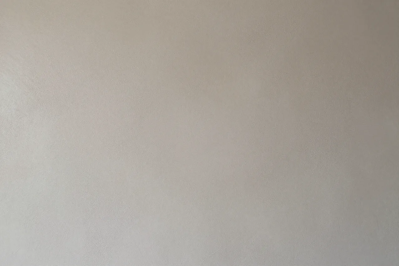 Full frame close-up of a smooth warm greige microcement wall surface with subtle texture