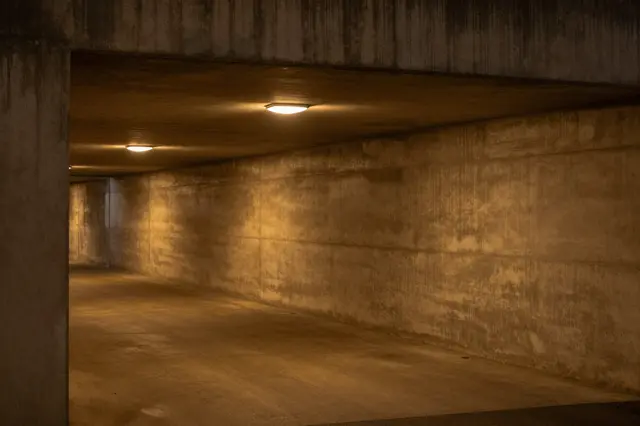 Empty raw concrete pedestrian underpass lit by warm amber ceiling lights at night