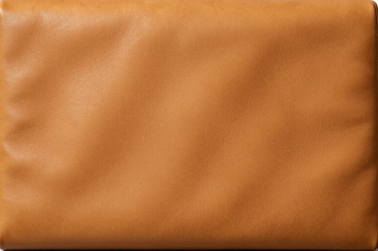 Full frame close-up of honey-toned worn leather with soft natural creases and subtle patina