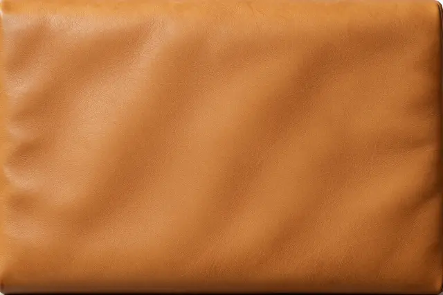Full frame close-up of honey-toned worn leather with soft natural creases and subtle patina