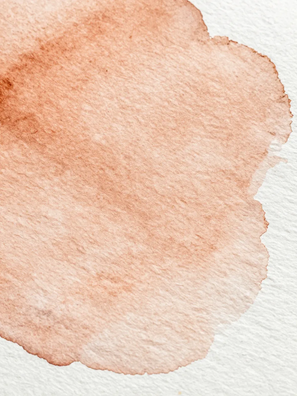 Close-up of textured watercolor paper with a soft dried warm ochre wash spread across its grain