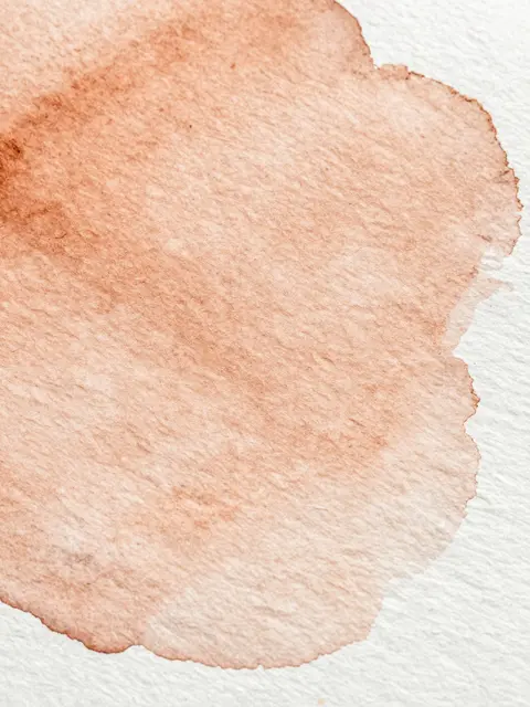 Close-up of textured watercolor paper with a soft dried warm ochre wash spread across its grain