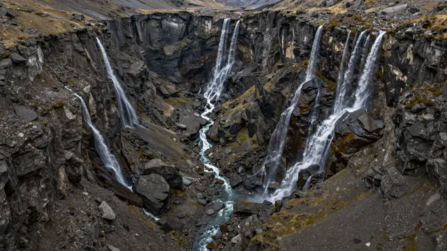 Multiple cascading waterfalls tumble down steep rocky walls of a U-shaped glacial valley into a central stream
