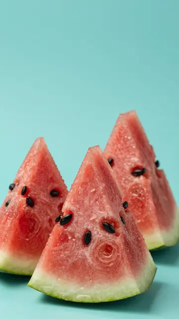 Three fresh triangular watermelon wedges sit against a solid turquoise backdrop
