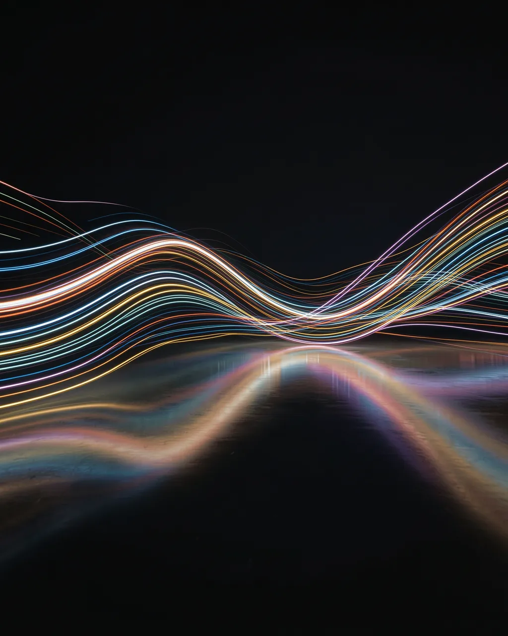 Wavy multicolored light trails curve over a glossy dark reflective floor against a solid black background