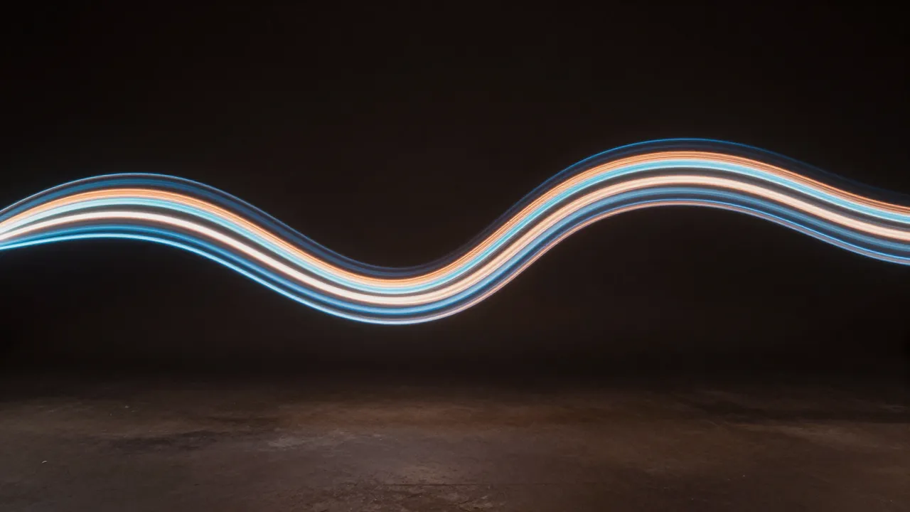 Smooth layered blue and warm orange light trails curve in a wave shape across a dark studio background