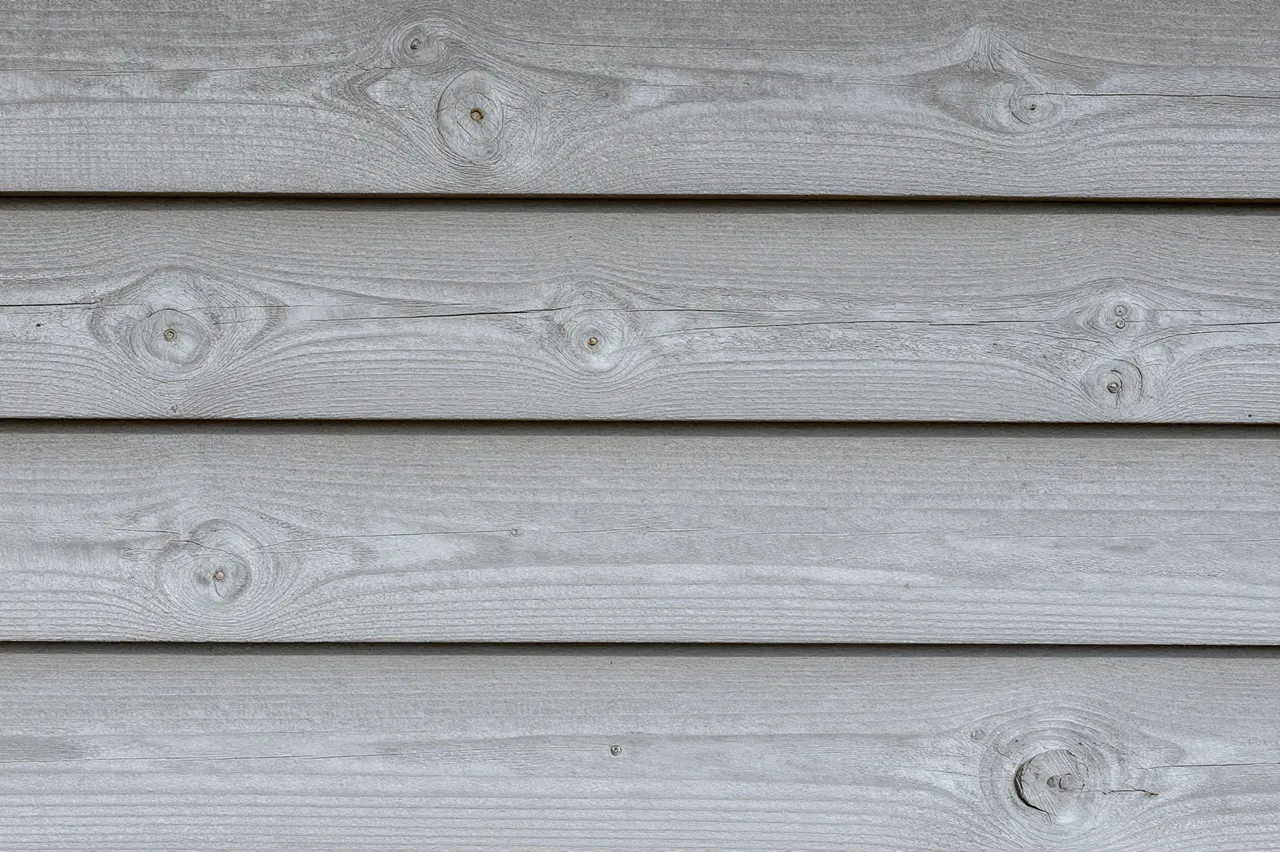 Close-up of horizontal weathered gray painted wood planks with visible knots and nail holes