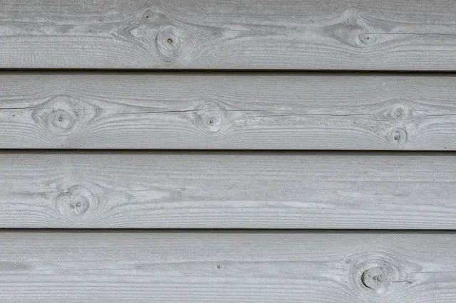 Close-up of horizontal weathered gray painted wood planks with visible knots and nail holes