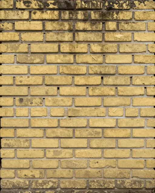 Full frame close-up of worn reclaimed yellow brick with soot marks and chipped edges under flat even light