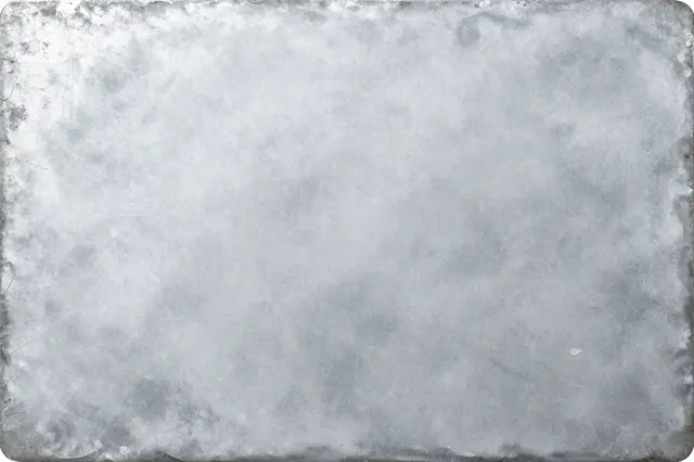 Full frame close-up of a zinc sheet with white oxidation bloom and soft gray mottling under flat even light