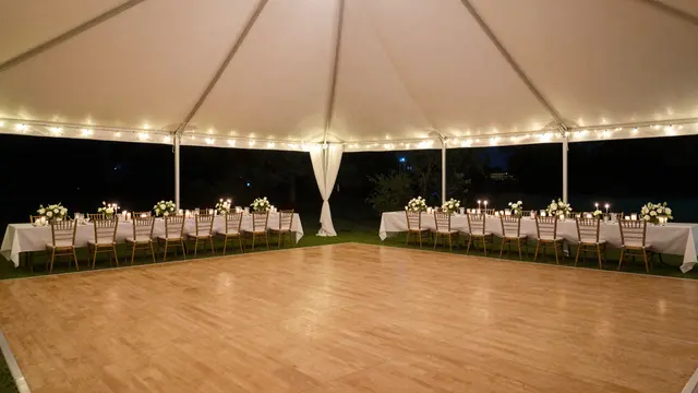 Empty lit wedding reception tent at night with long tables, fairy lights, and a wooden dance floor