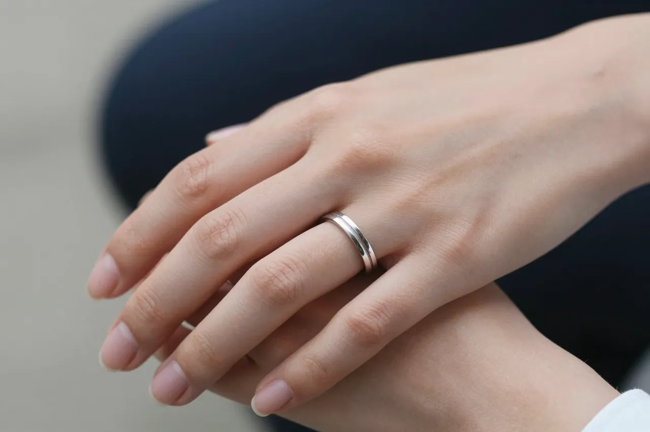 Close-up of two stacked hands, one displaying a simple silver wedding band on its ring finger