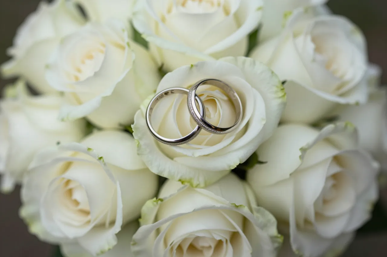 Two silver wedding rings rest on the center of a lush bouquet of creamy white roses.