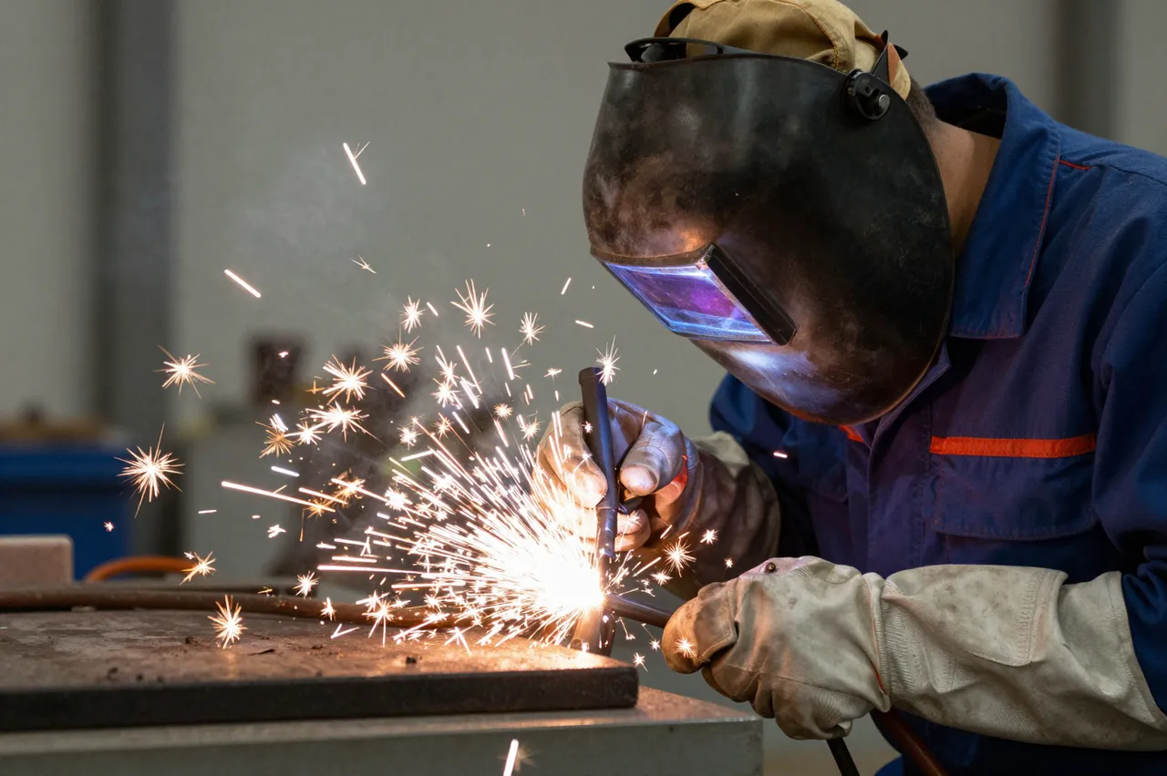A welder with a downed face shield creates bright sparks while welding metal in a workshop