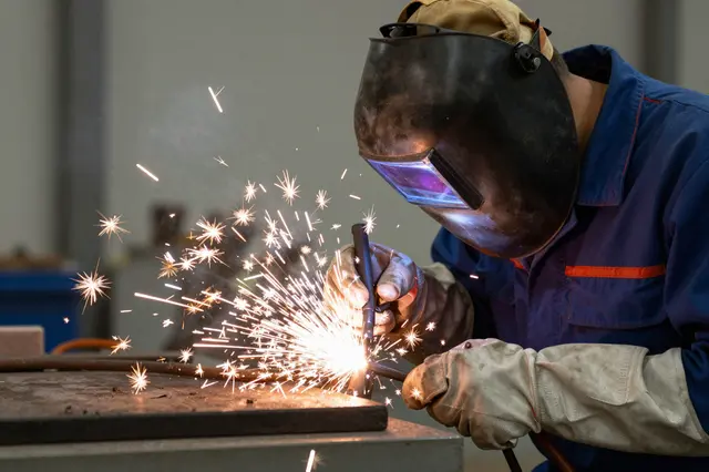 A welder with a downed face shield creates bright sparks while welding metal in a workshop