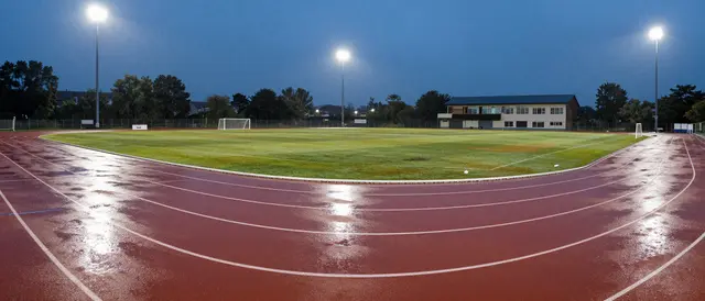 Empty rain-soaked running track with floodlight reflections at blue hour dusk