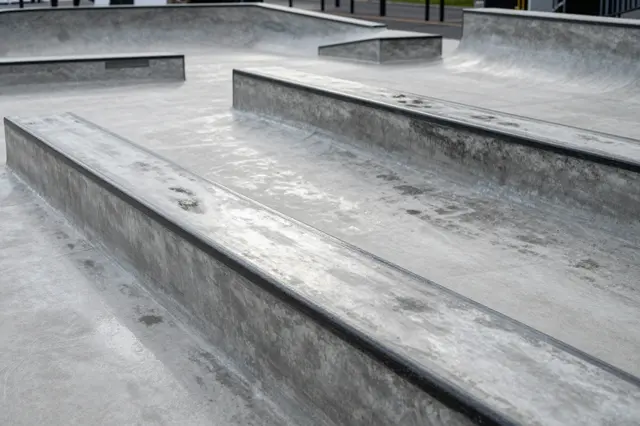 Clean wet gray concrete skate plaza with ledges and ramps after recent rain, empty of people