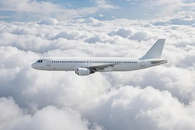 Unmarked white modern airliner flies in side view above a thick layer of fluffy white clouds in bright daylight.