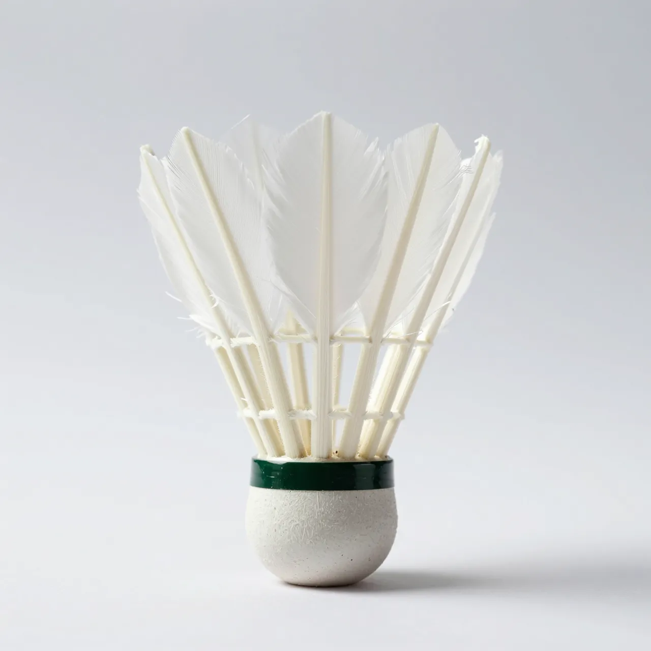A feather badminton shuttlecock stands upright on its cork base against a plain light gray studio background