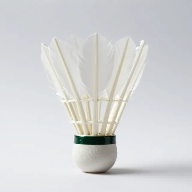 A feather badminton shuttlecock stands upright on its cork base against a plain light gray studio background
