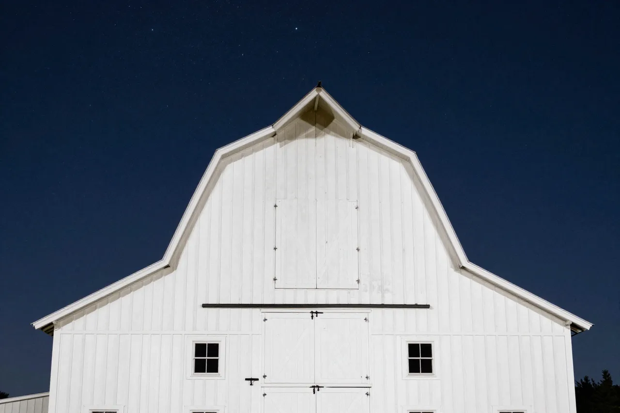 Front facade of a white gambrel barn beneath a dark star-dusted night sky