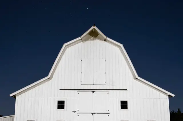 Front facade of a white gambrel barn beneath a dark star-dusted night sky