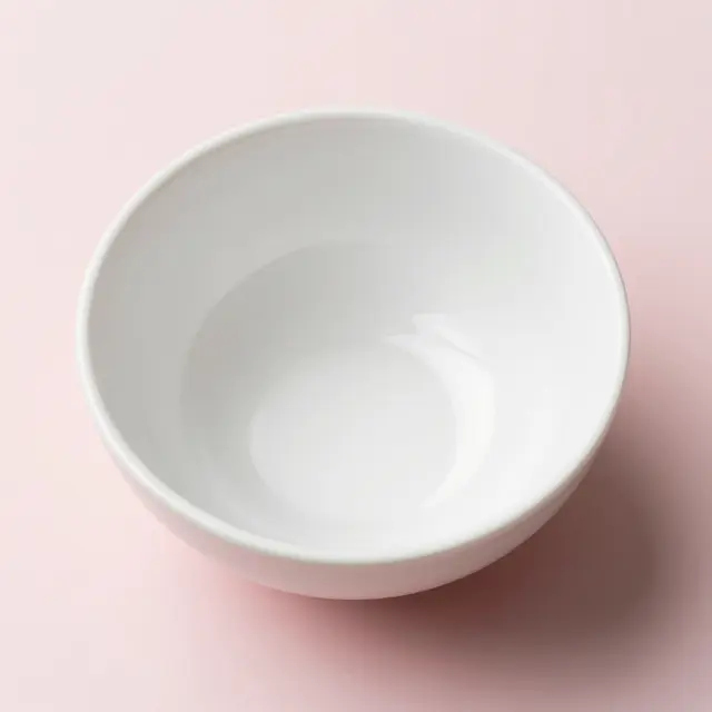 Top view of an empty plain white ceramic bowl resting on a soft pale pink background
