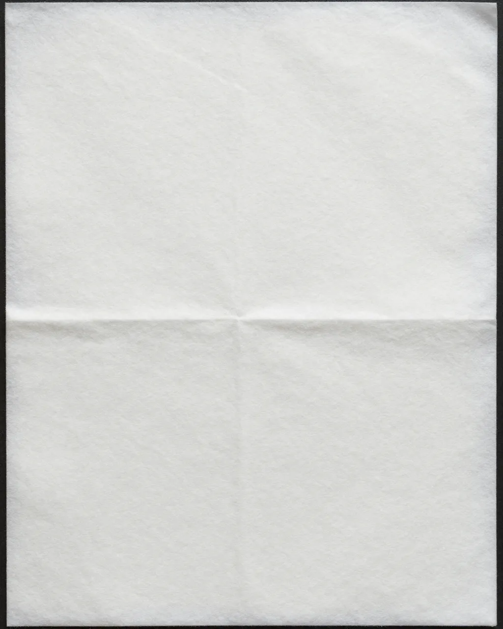 Full frame close-up of soft white matte blotting paper with faint fold creases against a thin dark border