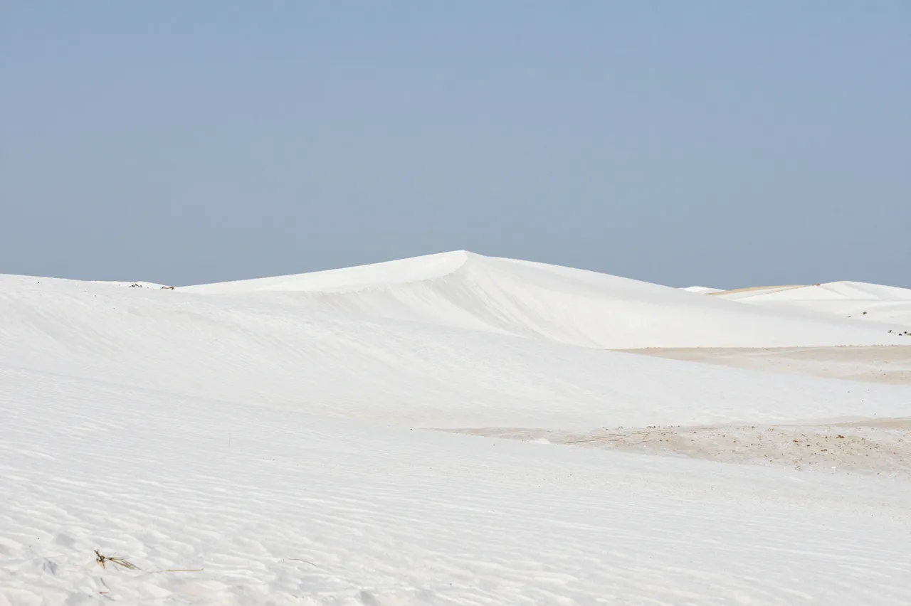 Smooth white gypsum sand dunes stretch beneath a clear pale blue sky