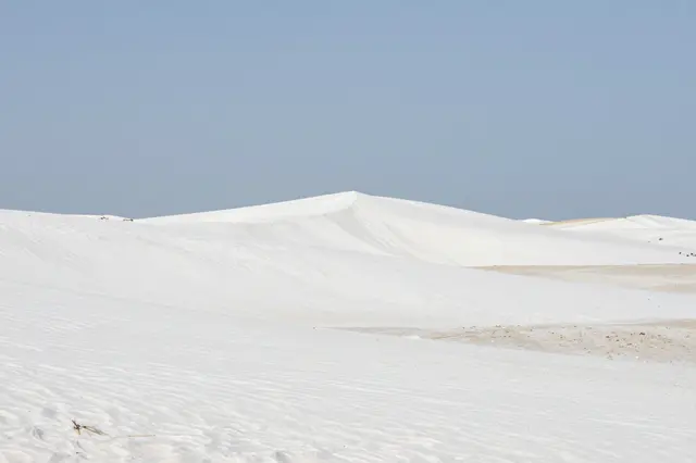 Smooth white gypsum sand dunes stretch beneath a clear pale blue sky