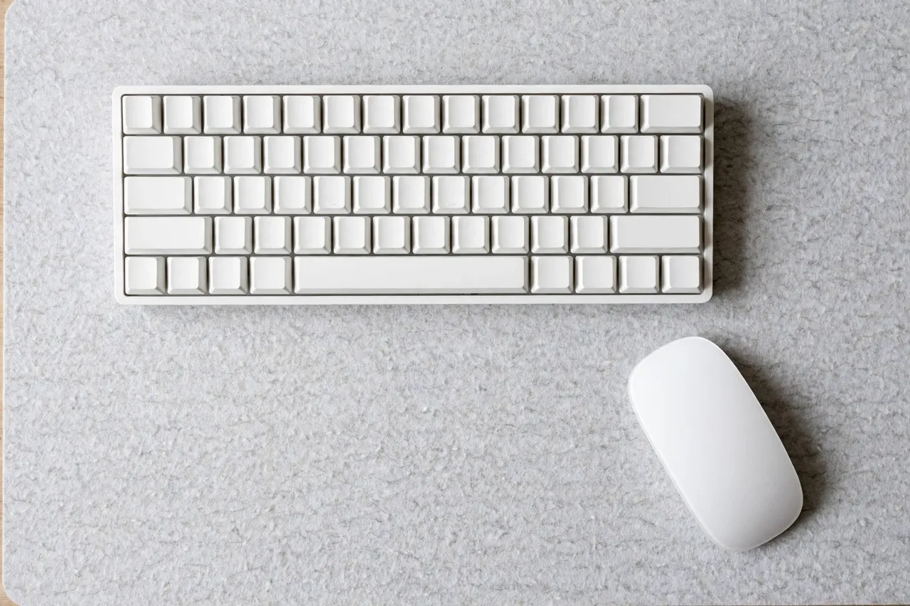 Overhead view of a blank white mechanical keyboard and white mouse resting on a light gray felt desk mat