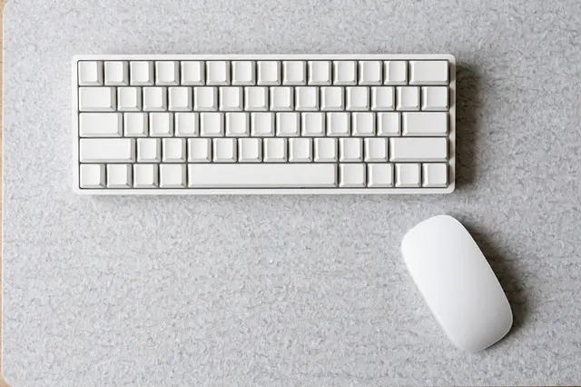 Overhead view of a blank white mechanical keyboard and white mouse resting on a light gray felt desk mat