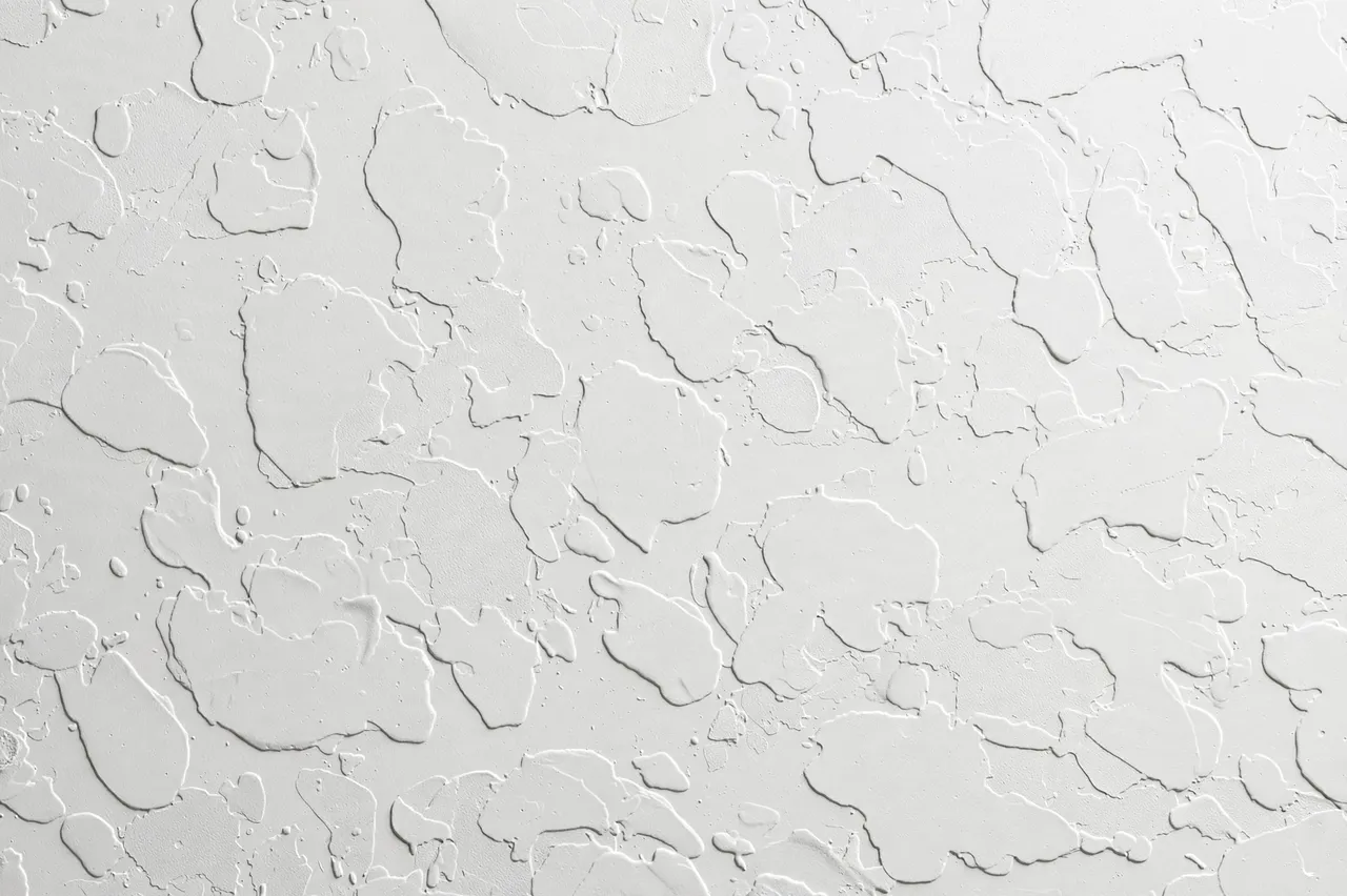 Full frame close-up of white knockdown plaster drywall texture with raised splatter blobs and smooth gaps