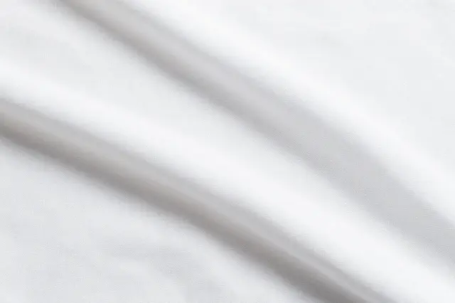 Top view of soft folded white linen fabric with gentle natural shadows and empty copy space