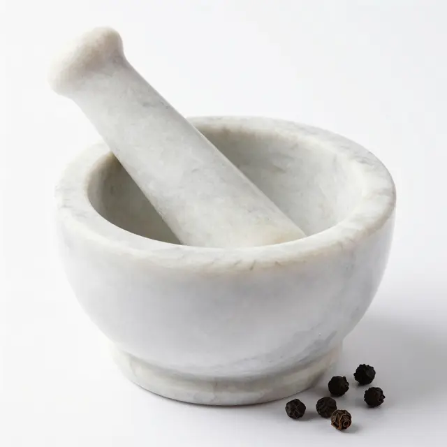 A white marble mortar and pestle with scattered black peppercorns rests on a plain white studio background.