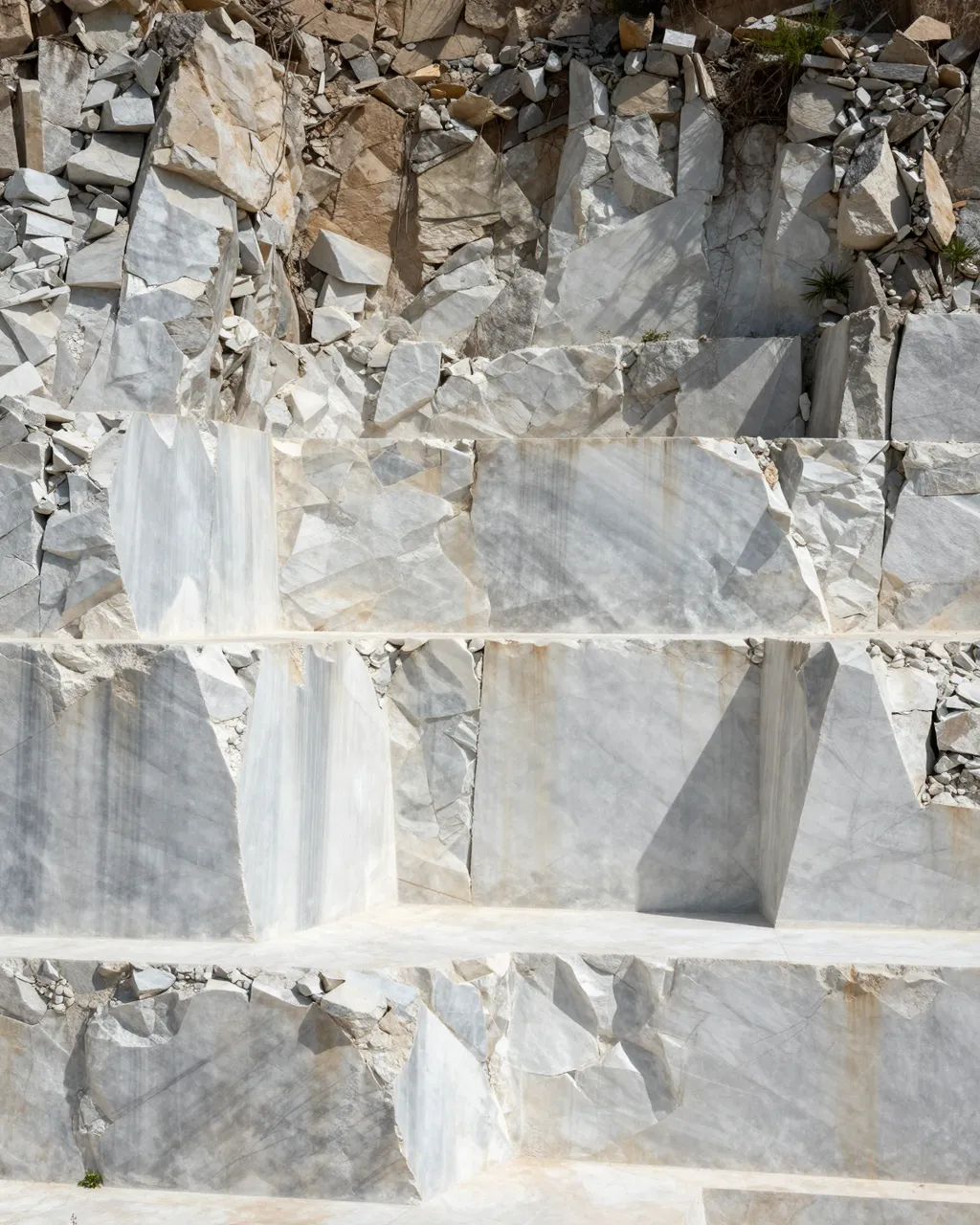 Stepped cut walls of a sunlit white marble quarry with scattered rock debris
