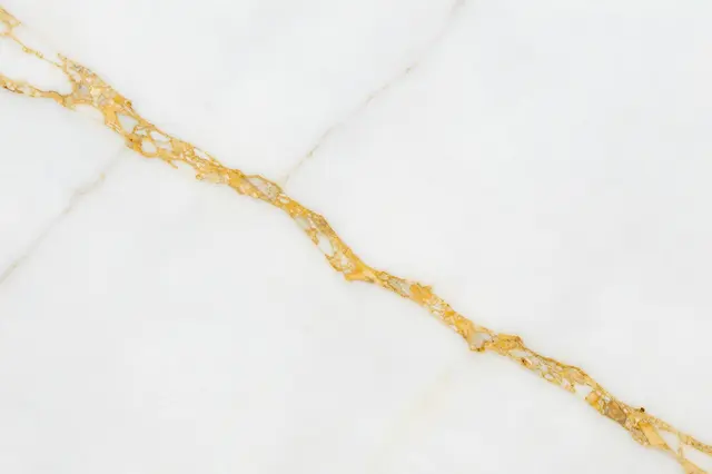 A close-up view of a polished white marble surface with flowing golden-brown veins