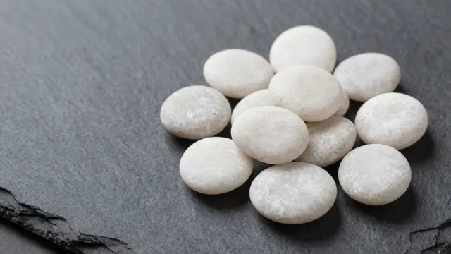 Cluster of smooth white pebbles sits on the right of a dark charcoal slate surface with empty copy space on the left.