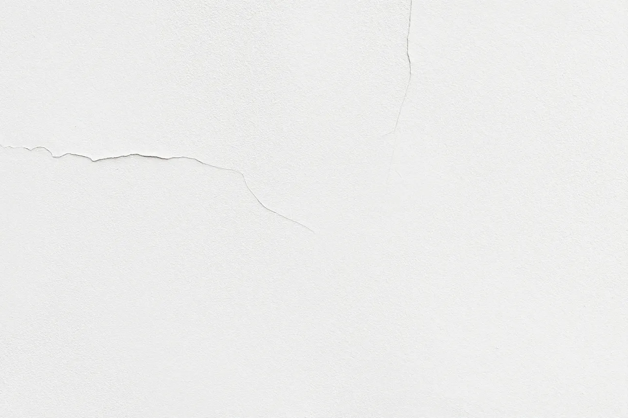 Smooth white plaster wall with subtle, thin natural cracks across its surface