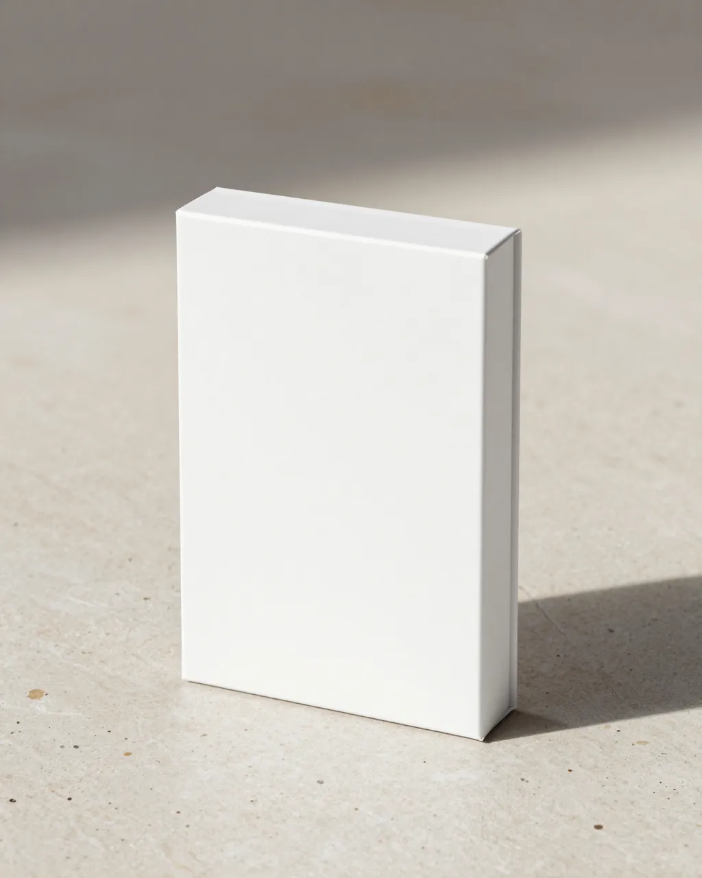 A blank upright white rectangular box rests on a light beige stone surface with a soft cast shadow