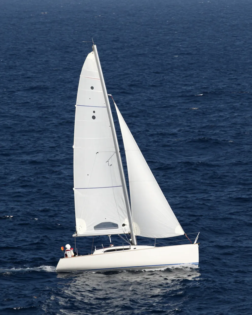 A white hulled sailboat with full sails heels as it travels across a dark deep blue ocean.