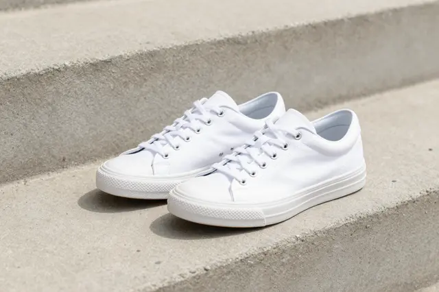Pair of plain white canvas sneakers resting on a light concrete step in soft sunlight