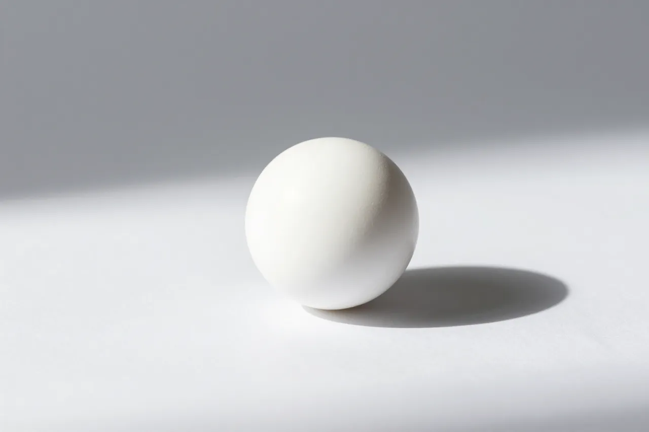 A smooth white sphere rests on a plain white surface casting a soft long shadow