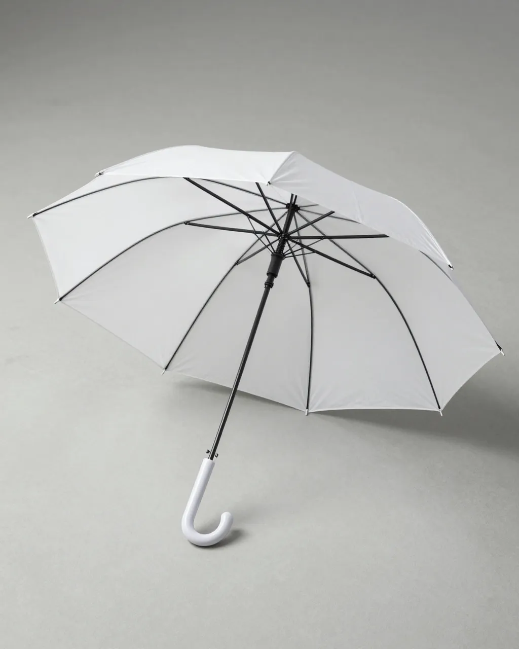 An open plain white umbrella rests on a smooth light gray studio floor