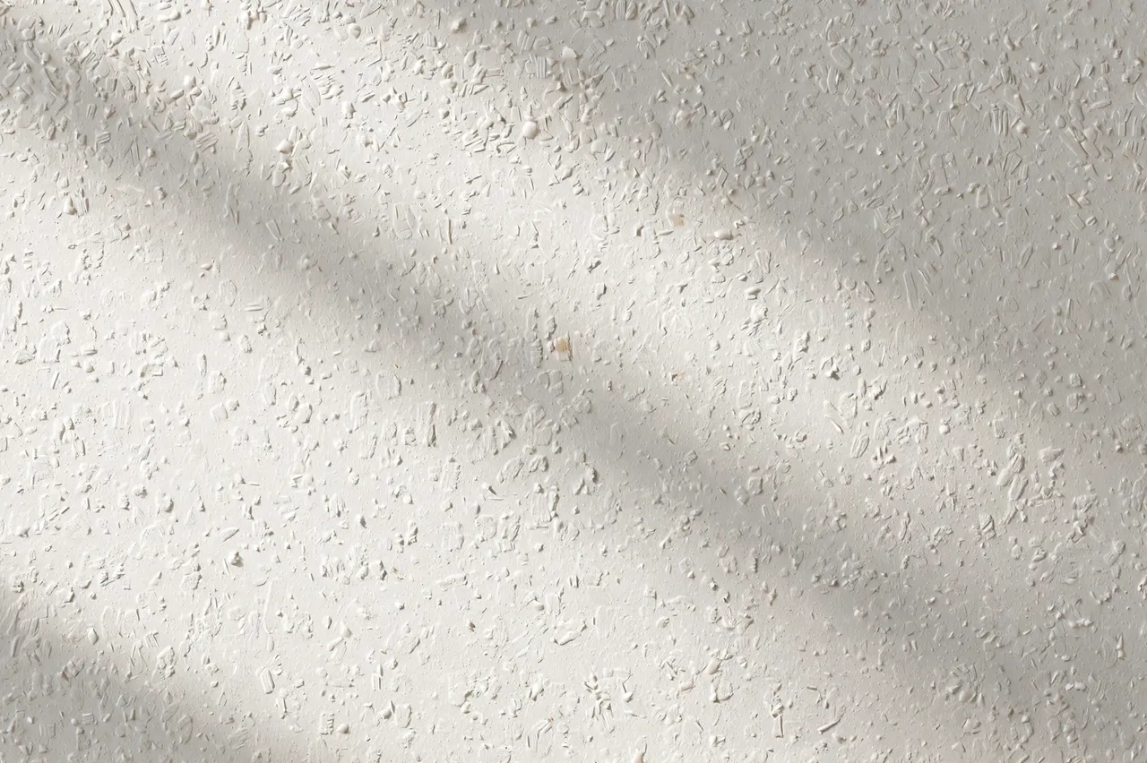 Full frame close-up of textured white painted woodchip wallpaper with soft raking light across the surface