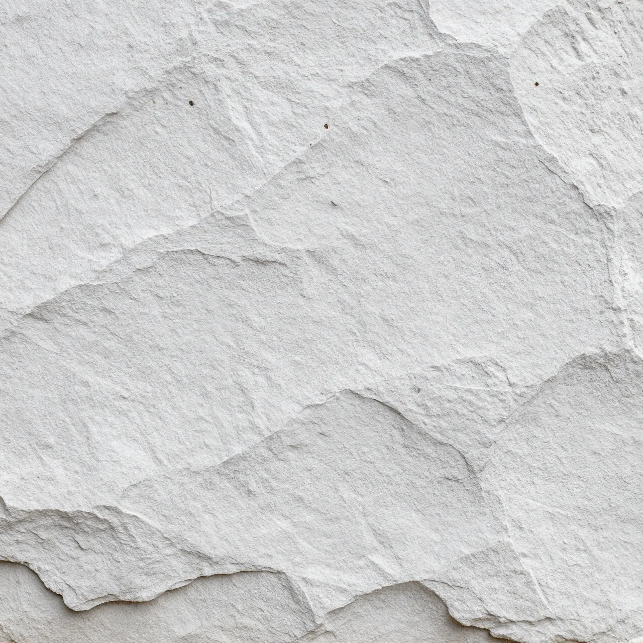 Full frame close up of rough gray stone covered in a thin, chalky whitewash coat under even flat light