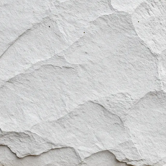 Full frame close up of rough gray stone covered in a thin, chalky whitewash coat under even flat light