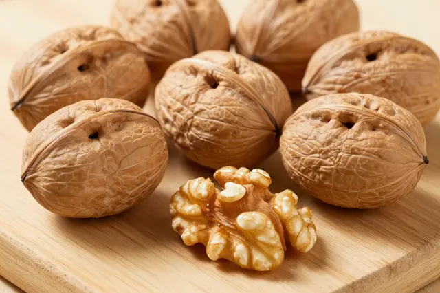 Whole in-shell walnuts and one shelled walnut kernel rest on a light wooden board