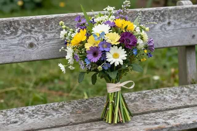 Hand-tied mixed garden flower bouquet rests on a weathered wooden cottage garden bench