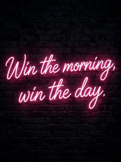 Glowing pink neon script sign reading "Win the morning, win the day." mounted on a dark brick wall at night